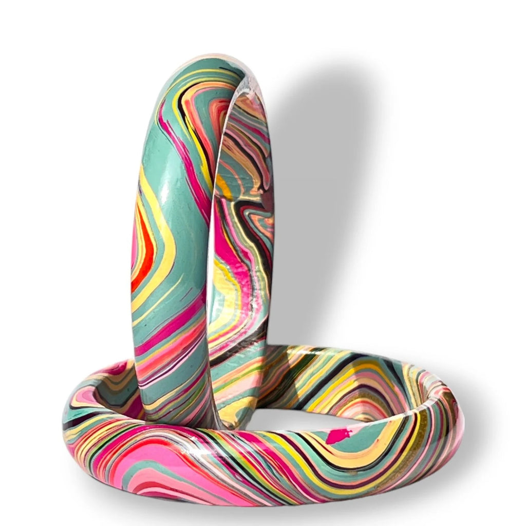A pair of thick bangle bracelets with a vibrant, swirling marbled pattern in pink, yellow, teal, orange, and black, displayed on a clean white background.