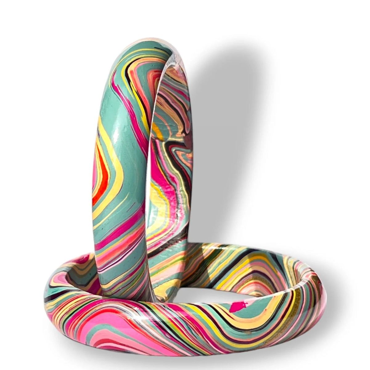 A pair of thick bangle bracelets with a vibrant, swirling marbled pattern in pink, yellow, teal, orange, and black, displayed on a clean white background.